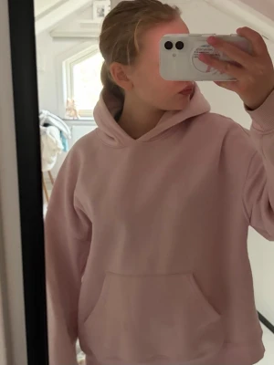 Ljusrosa hoodie med tryck - Säljer en ljusrosa hoodie med stor ficka framtill och huva. På ryggen står det 'SEE YOU IN PARIS' i stora röda bokstäver. Hoodien har en avslappnad passform och är gjord i mjukt material, perfekt för chill dagar.