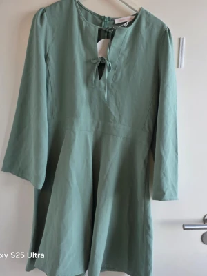 Grön klänning från See By Chloé - Stilren ljusgrön klänning från See By Chloé med trekvartsärm och knytning framtill vid halsen. Klänningen har en mjuk, lätt utsvängd form och dragkedja i ryggen. Perfekt för dig som gillar enkel men elegant design.