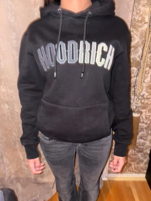 Svart HOODRICH hoodie med tryck - Bra skick, bra till kalla sommar dagar, passar både tjejer och killar, mjukt och skönt material på insidan. Jag säljer den eftersom att den är för stor för mig. Priset går att diskuteras