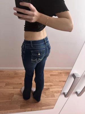 Y2K liknande jeans lågmidjade - Snygga mörkblå bootcut jeans med vita kontrastsömmar och dekorativa fickor bak. Jeansen har låg midja och klassisk femficksdesign. Perfekta för dig som gillar en retroinspirerad look och vill sticka ut med detaljerade sömmar. Passar även storlek L