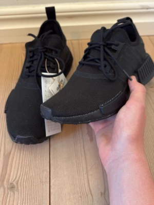 HELT NYA- Svarta Adidas NMD_R1 primeblue sneakers  - Helt nya Adidas NMD_R1 Primeblue svarta.  Aldrig använda, lappen sitter kvar.  Storlek 37 1/3    Säljer då de inte kom till användning    Pris kan diskuteras vid snabb affär