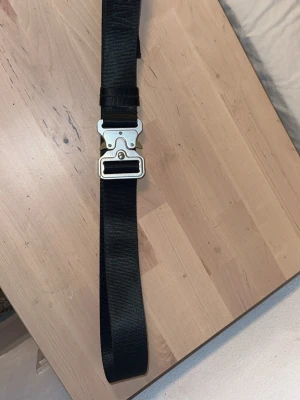 Black alyx belt - Säljer ett svart bälte från 1017 ALYX 9SM med deras ikoniska metallspänne. Bältet är gjort i slitstark syntet och har en cool, industriell känsla. Perfekt accessoar köpt på Grailed i 2020