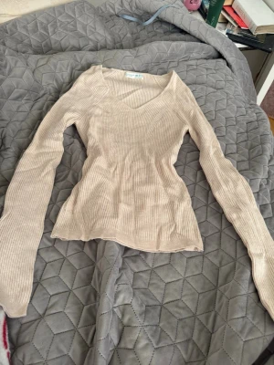 Beige ribbad långärmad topp - Snygg beige ribbad topp med v-ringning och långa ärmar. Figurnära passform och mjukt material som känns skönt mot huden. Perfekt att styla med jeans eller kjol för en trendig look.