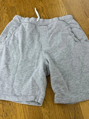 Grå sweatshorts med snörning - Grå mjuka sweatshorts från Religion Basics med snörning i midjan och två sidofickor. Perfekta för chill dagar eller träning. Liten logotyp-patch nertill på ena benet. Klassisk och enkel design i bomullsmix.