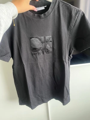 Svart Calvin Klein t-shirt - Svart t-shirt från Calvin Klein med broderad CK-logga på bröstet. Klassisk passform och rund halsringning, tillverkad i mjuk bomull. Perfekt för en stilren och enkel look.