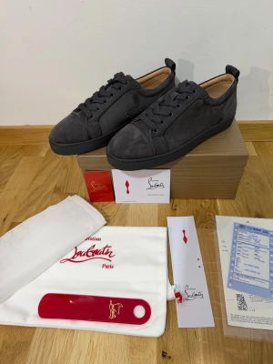Grå Mocka Loubs - Snygga mörkgrå sneakers i mocka från Christian Louboutin. Klassisk låg modell med rund tå, svarta skosnören och diskret logga på innersulan. Skorna har en stilren design och kommer med originalkartong, dustbag och tillbehör. TVEKA INTE ATT SKICKA EN BUD:)