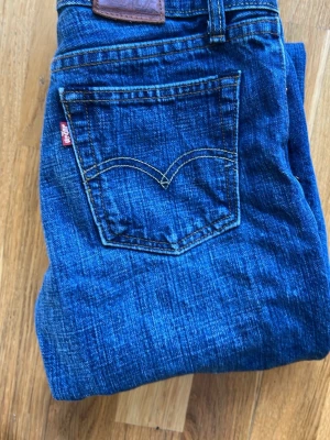 Levi's blå bootcut jeans - Säljer ett par klassiska blå Levi's jeans med bootcut passform. Jeansen har fem fickor, snygga kontrastsömmar och det ikoniska röda Levi's-märket på bakfickan. Perfekta för en avslappnad och tidlös stil.