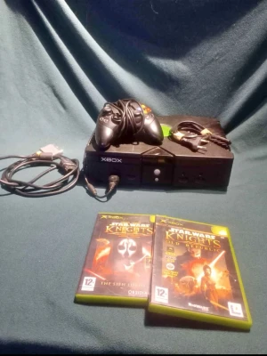 Xbox original med Star Wars-spel - Säljer en svart Xbox original med tillhörande handkontroll och kablar. Medföljer två spel: Star Wars Knights of the Old Republic I & II. Konsolen har en klassisk, robust design i plast och är perfekt för retrospelare som gillar äventyr och sci-fi.
