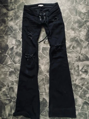 Utsålda jeans från Gina  - Säljer ett par svarta bootcut jeans med snörning i midjan och slitna detaljer på benen. Jeansen har väldigt midja och vida ben, vilket ger en snygg retrovibe. Har sytt ner så de är lite mer lågmidjade.  Tajta i låren, pris går att diskuteras 🤗Ska skriva alla måtten strax!❤️
