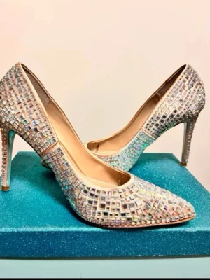 Blue by Betsey Johnson pumps - Ett par eleganta klackskor med spetsig tå. Skorna är prydda med glittrande stenar över hela ytan, vilket geren iögonfallande effekt. Klackarna är smala och höga, vilket bidrar till en sofistikerad silhuett. Perfekta för festliga tillfällen.