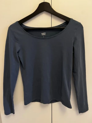 Blå långärmad topp från 157 - En basic blå långärmad topp från 157 med rund halsringning. Tillverkad i mjuk bomull med lite stretch för en skön passform. Perfekt att styla med jeans eller kjol för en enkel och clean look.