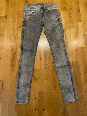 Grå skinny jeans från G-Star RAW stl 25 - Snygga grå skinny jeans från G-Star RAW, modell LYNN. Jeansen har en tvättad look, fem fickor och klassisk knappgylf. Perfekta för dig som gillar en slimmad passform och streetstyle-vibe.