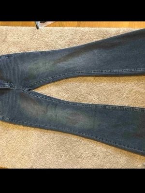 Blå bootcut jeans med slitningar - Säljer ett par blå bootcut jeans med lätt slitna detaljer och tvättade partier på låren. Jeansen har klassisk femficksmodell och normal midja. Materialet är stretchigt denim som sitter bekvämt och formar sig efter kroppen.