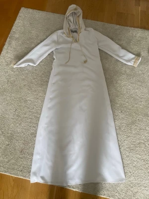 En elegant fin abaya  - Elegant och specialsydd abaya från Dubai i mycket fint skick. Vit med fina gulddetaljer vid ärmarna och huva. Bekväm och stilren modell med fint fall. Endast använd 1 gång. Perfekt för eid, speciella tillfällen eller vardagligt modest mode. 