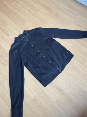 Hugo Boss sweatshirt/jacka – Strl S - Stilren svart sweatshirt/jacka från Hugo Boss med knappstängning framtill. Enkel och clean design som passar till det mesta. Bra skick och skön passform.  Storlek S Slim Fit. Modellen på bilden är ca 185 cm lång och väger ca 78 kg för referens.