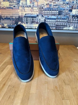 Blå mocka loafers från Sergio Ricci - Snygga loafers i blå mocka från Sergio Ricci med vit sula och klassisk slip-on design. Skorna har en stilren form och diskreta sömmar längs ovandelen. Perfekta för dig som gillar en clean och modern look.