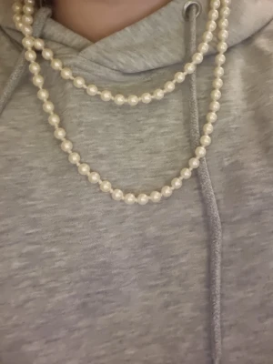Långt pärlhalsband i klassisk stil - Säljer ett långt halsband med vita pärlor i klassisk design. Halsbandet kan bäras i flera lager och ger en tidlös och elegant look. Perfekt accessoar för att lyfta din outfit med en touch av vintagekänsla.