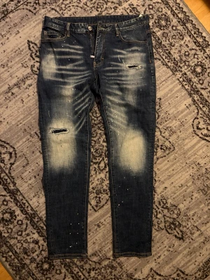 dsquared jeans - Säljer ett par mörkblå dsquared slim jeans med slitningar och hål på låret samt blekta partier framtill, utan dsquared röda märket. Storlek 52, motsvarar ksk 32W/32-33L
