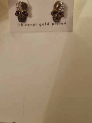 Dödskalleörhängen med kristaller - Coola örhängen i form av dödskallar, gnistrande stenar på huvudet. Snygg detalj för dig som gillar edgy accessoarer och vill sticka ut lite extra. Passar perfekt till streetstyle eller rockig look.