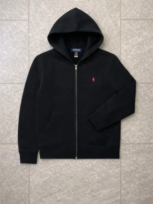 Ralph Lauren zip hoodie  - Säljer en svart Polo Ralph Lauren zip hoodie i stilren och clean design. 🖤  Klassisk modell med liten Ralph Lauren-logga på bröstet och hög kvalitet i materialet. Hoodien är bekväm, mjuk och sitter riktigt snyggt.  Storlek S/M.  Zip-up modell med huva och fickor framtill.  Bra skick och väldigt fräsch.  Skriv vid intresse eller frågor.
