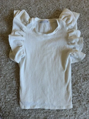 Vit topp med volangärmar från Zara - Säljer en vit söt topp från Zara med volangdetaljer på ärmarna❤️är i strl s men passar dom med xs också 