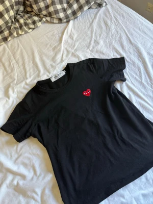 Svart t-shirt från Comme des Garçons - Svart t-shirt från Comme des Garçons PLAY med det ikoniska röda hjärtat med ögon broderat på bröstet. Klassisk rund hals och korta ärmar. Perfekt för dig som gillar stilrena plagg med en twist.
