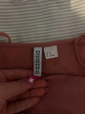Rosa linnetopp från H&M Divided - Säljer en söt rosa linnetopp från H&M Divided. Toppen är ärmlös med smala axelband och har en tight passform som sitter snyggt på kroppen. Perfekt att styla med jeans eller kjol för en trendig look.