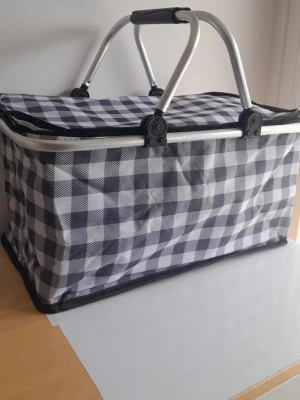 Stor isolerad picknickkorg - 30L kylväska med retromotiv - Denna bärbara kylväska på 30 liter är perfekt för familjeutflykter, stranddagar eller matinköp. Den har ett fantastiskt retroblommigt 70-talstryck i varma hösttoner (orange, gult och brunt).  Viktiga funktioner: Stor kapacitet: 30 liter (gott om plats för drycker, snacks och lunch). Isolerad insida: Håller mat och dryck svala eller varma i timmar.  Robust design: Lätt aluminiumram med ett bekvämt vadderat handtag.                            Mått: 40 cm x 23 cm x 30 cm (ca 15,7" x 9,05" x 11,8").