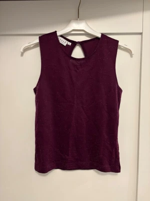 Glittrig vinröd ärmlös topp - Snygg vinröd ärmlös topp med glittriga detaljer och rund halsringning. Toppen har en liten öppning i nacken och är gjord i ett stretchigt material som känns mjukt mot huden. Perfekt för att lyfta vilken outfit som helst.