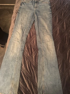 Ljusblå bootcut jeans - Säljer ett par ljusblå bootcut jeans med klassisk femficksmodell och normal midja. Jeansen har en lätt tvättad look och raka, utsvängda ben. Perfekta för dig som gillar retrostil och vill ha ett par bekväma jeans i bomull.