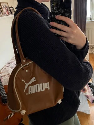Brun handväska från Puma - Cool brun liten handväska från Puma. Den är i bra bortsett från fodret på insidan som är något fläckigt, se bild 7 (har ej testat rengöra).
