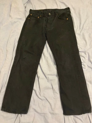 Svarta Levi's 501 jeans straight fit - Klassiska svarta Levi's 501 jeans med rak passform och knappgylf. Jeansen har fem fickor och är tillverkade i kraftig denim. Perfekta för en avslappnad och tidlös stil. Bara att skriva vid vidare frågor.