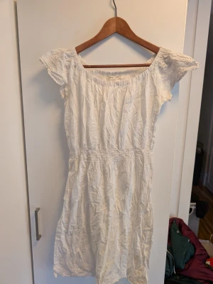 Vit kortklänning från Lager 157 Vintage - Söt vit klänning från Vintage med korta ärmar och smockdetaljer vid midjan och halsen. Klänningen har en luftig och enkel design, perfekt för varma dagar. Materialet är bomull och modellen är kortklänning med normal passning.Skrynklig då den legat nerpackad, behöver en tvätt.
