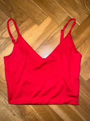 Röd croppad linnetopp - Snygg röd croppad linnetopp med smala axelband och v-ringad hals. Perfekt till jeans eller kjol för en trendig look. Tunn och mjuk i materialet, passar bra till varmare dagar.