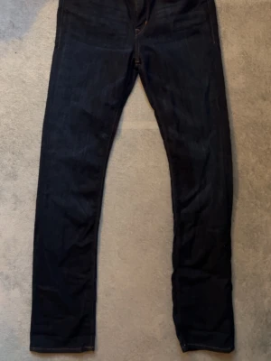 Mörkblå raka jeans från H&M och Denim - Säljer ett par mörkblå jeans med rak passform och klassisk femficksdesign. Jeansen har guldfärgade nitar och knappdetaljer samt kontrastsömmar. Perfekta till en avslappnad streetwear-look.