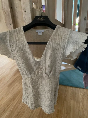 Beige topp - Säljer en beige topp med v-ringning och korta, vågiga ärmar. Den är snached vid midjan formas efter kroppen, otroligt snygg! Säljer då den inte kommer till användning. Den har inga skavanker💕