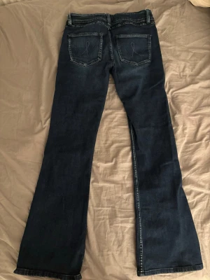Mörkblå bootcut jeans med brodyr från gina tricot🫶🏻 - Säljer ett par mörkblå bootcut jeans med snygg broderad detalj på bakfickorna. Jeansen har klassisk femficksdesign, normal midja och utsvängda ben. Perfekta för dig som gillar en retroinspirerad look och vill ha ett par jeans som sticker ut lite extra. Supersnygga!🤍