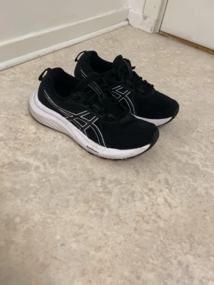  Asics sneakers  - Säljer ett par svarta Asics sneakers med vit sula och klassiskt Asics-mönster i vitt på sidorna. Skorna har meshmaterial för bra ventilation och snörning framtill. Perfekta för dig som gillar sportig stil och komfort.