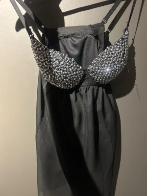 Svart klänning med glittrig topp - Supersnygg svart kortklänning med glittrig paljett-topp och tunna axelband. Klänningen har en tight överdel med massor av silverfärgade paljetter och en lätt, flowy kjol. Perfekt för dig som vill sticka ut och glänsa på festen! Super snygg verkligen. Skulle säga att kuporna är b-c kupa. Skriv för mer frågor, priset går att diskutera💕