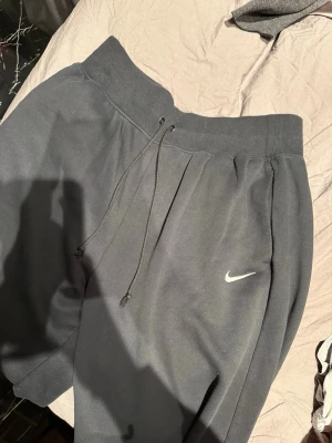 Svarta mjukisbyxor från Nike - Snygga svarta mjukisbyxor från Nike med klassisk vit logga på benet. Byxorna har bred resår i midjan, dragsko och raka ben. Tillverkade i mjukt material som känns skönt mot huden. Perfekta för en avslappnad och sportig stil. Modellen tall 