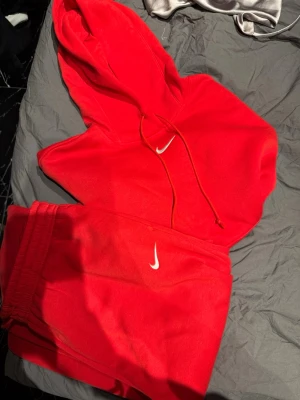 Nike mjukis/träning set oanvänt  - Snygg röd hoodie från Nike med klassisk vit logga på bröstet. Hoodien har huva med dragsko och en stor magficka framtill. Perfekt för en sportig och avslappnad stil. Mjukt material som känns skönt mot huden. Byxorna är storlek L och tröjan M kostar 1409 nytt endast använt 2 gånger då dem är för stora 