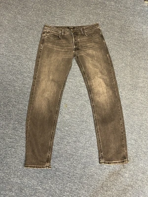 Grå tapered jeans från Jack & Jones - Säljer ett par gråa tapered jeans från Jack & Jones, modell Mike. Jeansen har en snygg tvättad look med ljusare partier och klassisk femficksdesign. Perfekta för dig som gillar en avslappnad men ändå stilren stil.