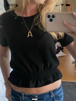 Svart croppad fest topp - Svart croppad topp med korta ärmar och resår i midjan som ger en snygg rynkad effekt. Enkel och stilren design, perfekt att matcha med jeans eller kjol. Mjuk och skön bomullskänsla.