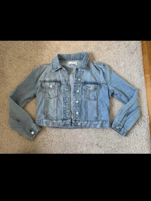 Ljusblå klassisk jeansjacka - Snygg ljusblå jeansjacka med raka linjer och klassisk krage. Jackan har två bröstfickor med lock och silverfärgade knappar framtill.