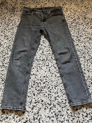 Jeans 29/30 - Säljer ett par grå jeans från Acne Studios med rak passform och klassisk femficksdesign. Jeansen har en snygg tvättad look och är tillverkade i kraftig denim. Perfekta för dig som gillar stilrena och tidlösa plagg.