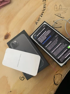 iPhone med svart box och trippelkamera - Säljer en iPhone från Apple med elegant svart box. Mobilen har trippelkamera på baksidan och stilren design i glas och metall. Perfekt för dig som vill ha en kraftfull smartphone med snygg look och avancerad kamerateknik.