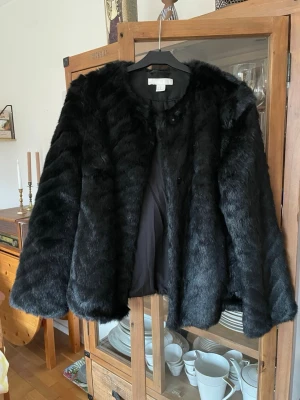 Svart jacka i fuskpäls från H&M - Jättefin och elegant jacka med knappar och fickor. Den är endast använd någon enstaka gång, nära nyskick. Storlek XS, men har för mig den passar S också. Mått går att få vid intresse. Mjuk och skön!