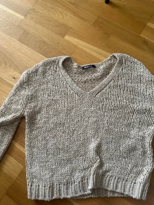 Beige stickad tröja med v-ringning - Säljer en beige stickad tröja från Gina Tricot med v-ringad hals och grovstickat mönster. Tröjan har långa ärmar och ribbade muddar vid ärmslut och nederkant. Perfekt för lager på lager och en avslappnad look.