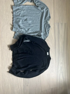 Grå och svart stickad tröja - Två stilrena stickade tröjor i grått och svart. Båda har rund halsringning, långa ärmar och ribbade muddar vid ärmslut och nederkant. Perfekta basplagg för lager på lager och passar till det mesta i garderoben.strl 170 vilket motsvarar XS