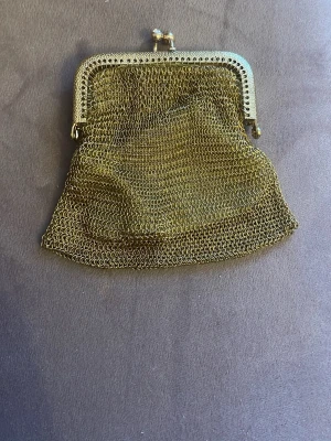 Guldig metallnät plånbok retro - Säljer en liten plånbok i guldigt metallnät med klassiskt snäpplås. Plånboken har en unik vintagekänsla och är perfekt för mynt eller småsaker. Den har en mjuk, flexibel form och glänsande finish som sticker ut i mängden.